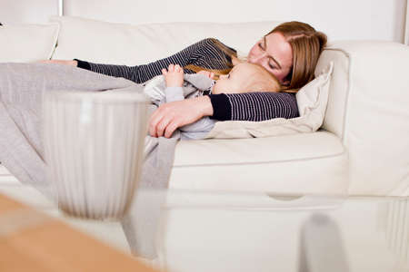 Baby girl and mother resting on sofa