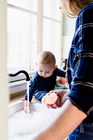 Baby boy touching running water at kitchen sinkの写真素材