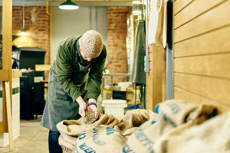 Male coffee shop owner checking raw coffee beans in store roomの写真素材