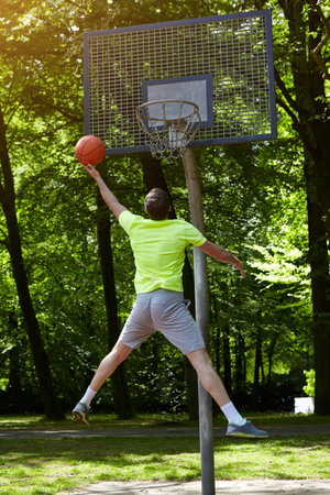 Rear view of young male basketball player jumping and throwing ball at basketball hoop