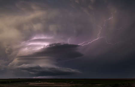 Powerful electrical storm with lightning arcing out of the updraft into the anvil and a...