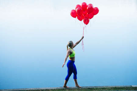 Side view of woman holding bunch of red balloonsの写真素材