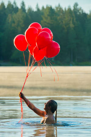 Woman in water holding bunch of red balloons