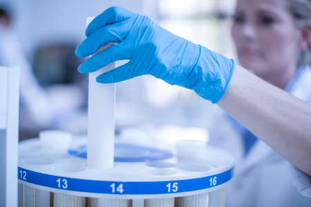 Mid adult woman in laboratory inserting test tube into tray