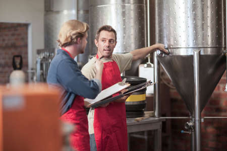 Colleagues in microbrewery discussing conical tankの写真素材