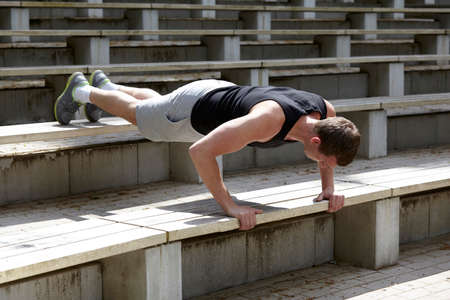 Young man training, doing push ups on stadium stairway