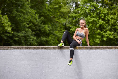 Young woman training, portrait sitting on top of wallの写真素材