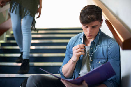 Young male college student sitting on stairway reading fileの写真素材