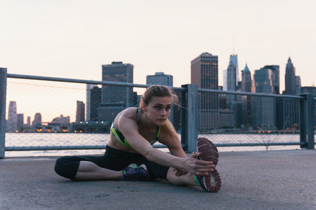 Young woman exercising outdoors, stretching by waterfront, Brooklyn, New York, USAの写真素材