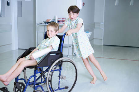 Boy patients pushing friend in wheelchair  on hospital children's wardの写真素材