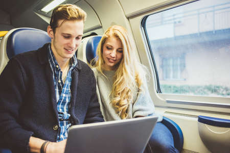 Young couple typing on laptop whilst travelling in train carriage, Italyの写真素材
