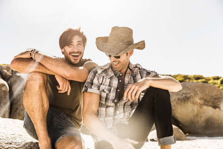 Two men laughing whilst sitting on beach, Cape Town, South Africa