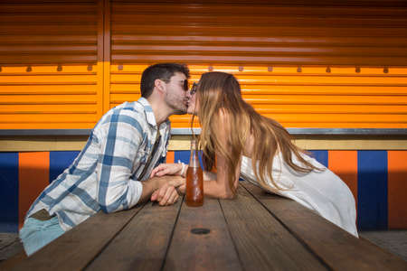 Couple sitting face to face at picnic table kissing, Coney island, Brooklyn, New York, USAの写真素材