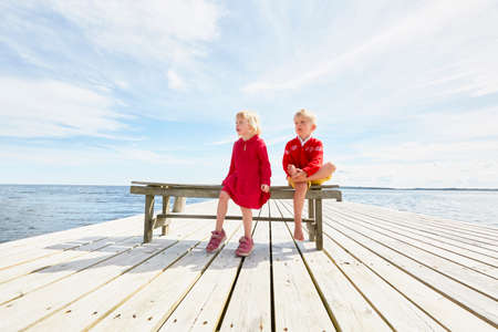 Two young friends sitting on bench on wooden pierの写真素材