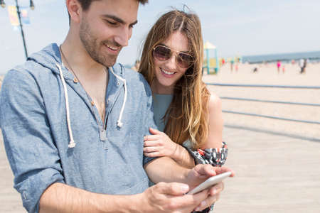 Couple looking at smartphone smiling, Coney island, Brooklyn, New York, USAの写真素材