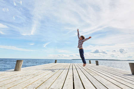 Young boy on wooden pier, jumping to reach bubbles