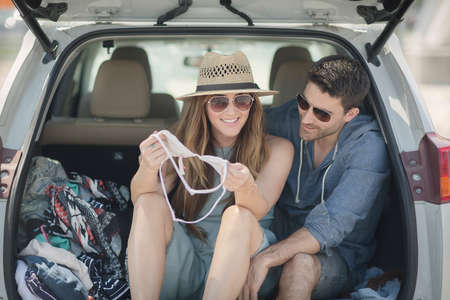 Couple in car boot looking at bikini top smilingの写真素材