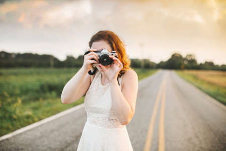 Woman on rural road taking photograph using camera