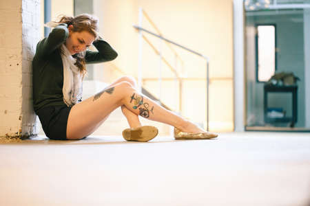 Side view of tattooed woman sitting against wallの写真素材