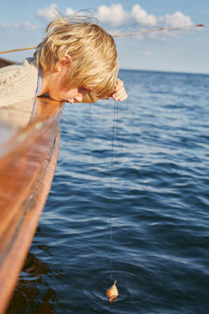 Boy dangling fishing float from boat