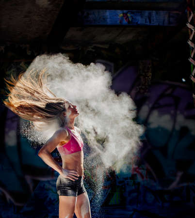 Woman standing with hands on hips throwing powder covered hair backの写真素材