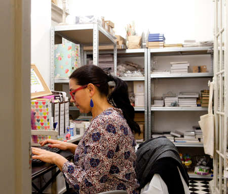 Female small business owner typing on computer keyboard in gift shop stockroomの写真素材