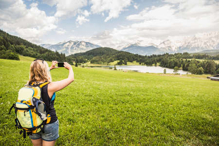 Woman taking photograph of Karwendel mountains, Gerold, Bavaria, Germanyの写真素材