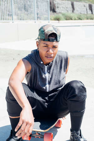 Woman sitting on skateboard looking at cameraの写真素材