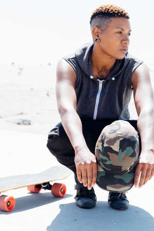 Woman crouching by skateboard looking awayの写真素材