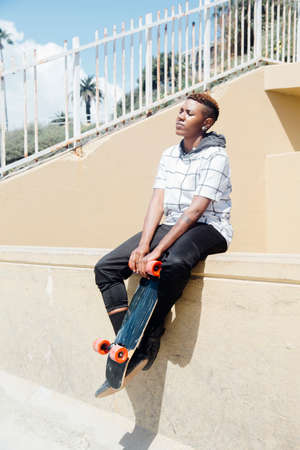Woman sitting on wall holding skateboard, eyes closedの写真素材