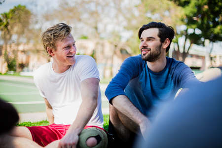 Group of male friends sitting together in park, laughingの写真素材