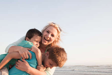 Mother by ocean hugging sons smilingの写真素材