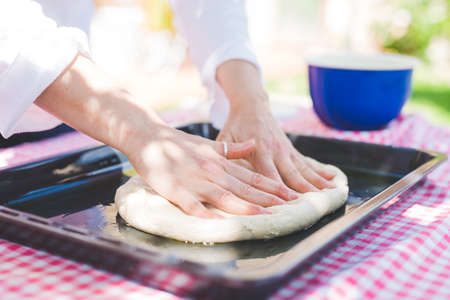 Woman's hands kneading dough on baking tin in garden