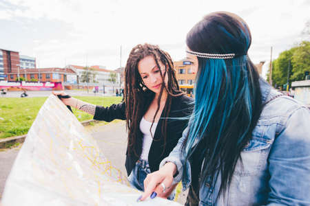 Two young women with dreadlocks and dyed hair pointing at map in urban parkの写真素材