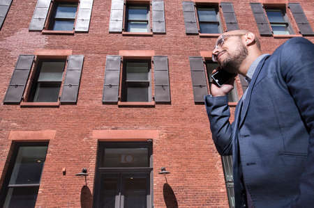 Businessman walking outdoors, using smartphone, low angle viewの写真素材