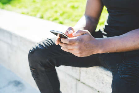 Young man, outdoors, holding smartphone, low section