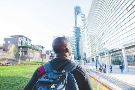 Young man walking outdoors, wearing backpack, rear view