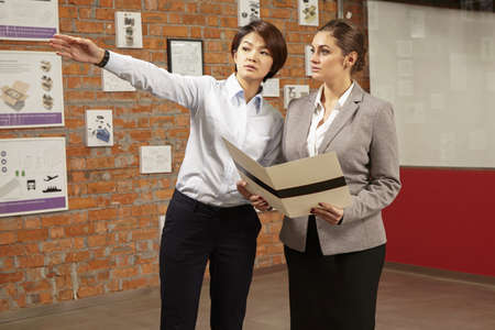 Female asian worker showing prints to caucasian female manager in gallery of printing and packaging...