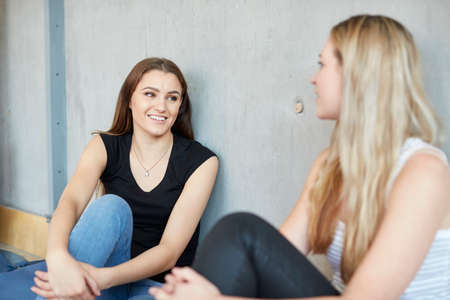 Two young female students sitting on floor chatting at higher education collegeの写真素材
