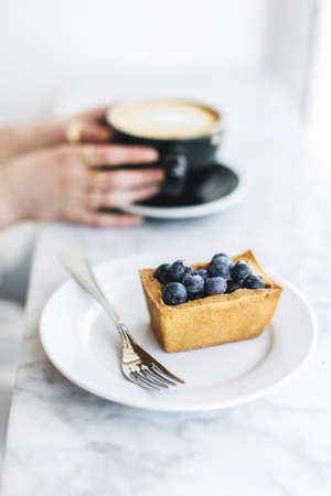 Fruit tart and woman's hands holding frothy coffeeの写真素材