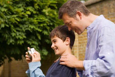 Mature man explaining digital camera to son in gardenの写真素材