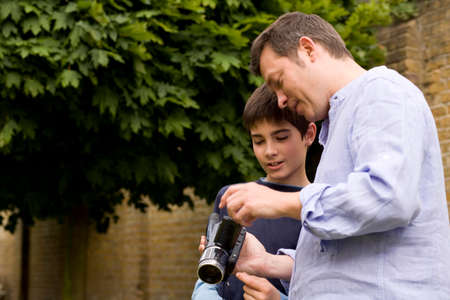 Mature man explaining video camera to son in garden