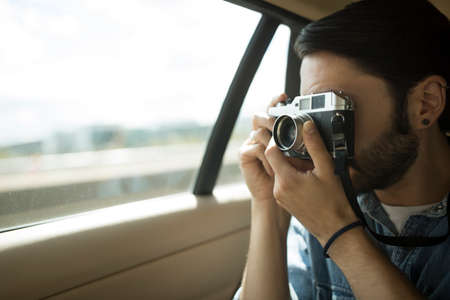 Young man on the road, taking photographs through car windowの写真素材