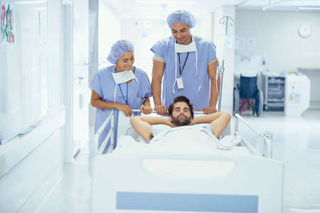 Young male patient in hospital bed being pushed by nurses