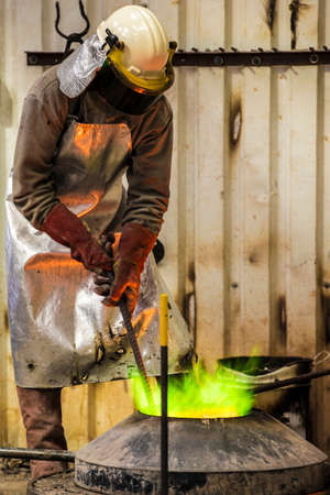 Male foundry worker working with green flamed furnace in bronze foundry