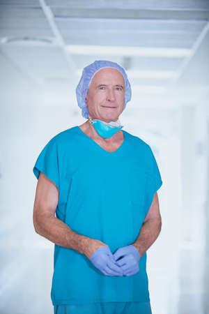 Portrait of senior male medic wearing scrubs in hospital corridorの写真素材