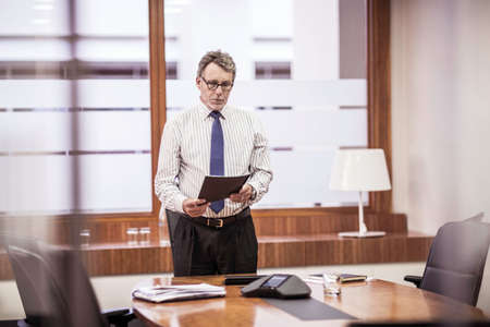 Senior businessman reading paperwork at boardroom tableの写真素材