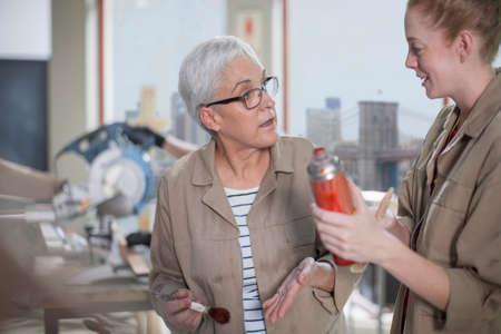 Mature female carpenter explaining wood stain to trainee in furniture making workshop