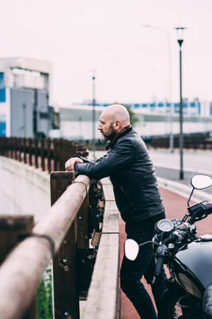 Mature male motorcyclist looking out from roadside railingの写真素材
