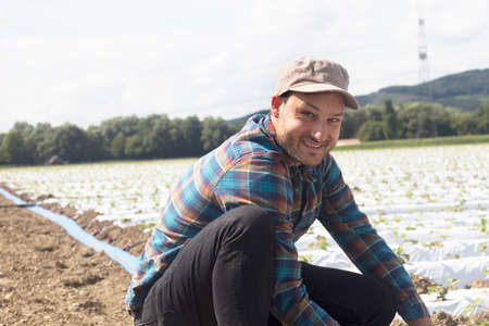 Farmer in field tending to seedlings, looking at camera smilingの写真素材